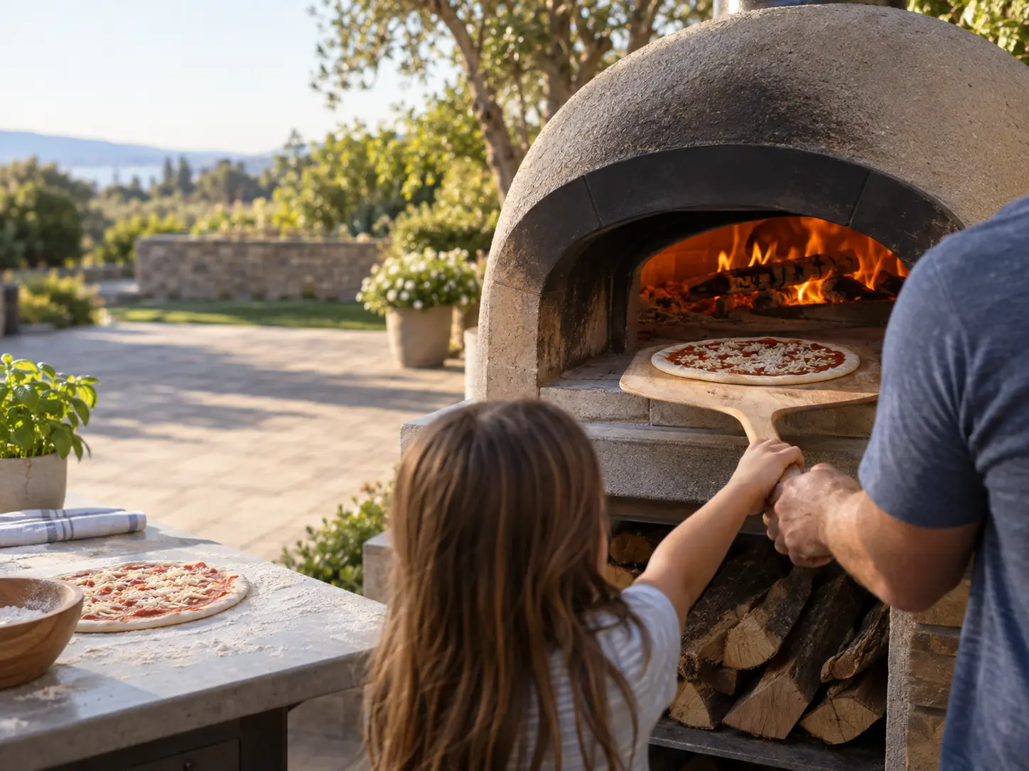 A family sliding a pizza into a wood-fired pizza oven on a sunny patio.