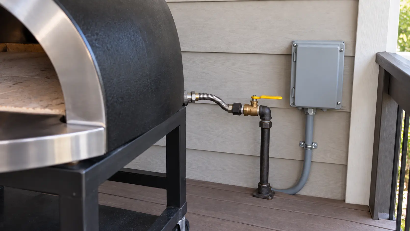 Close on a gas shutoff valve and an electrical box behind a deck pizza oven.